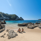 A couple lounges in a sandy cove surrounded by cliffs © Ascent / Getty Images