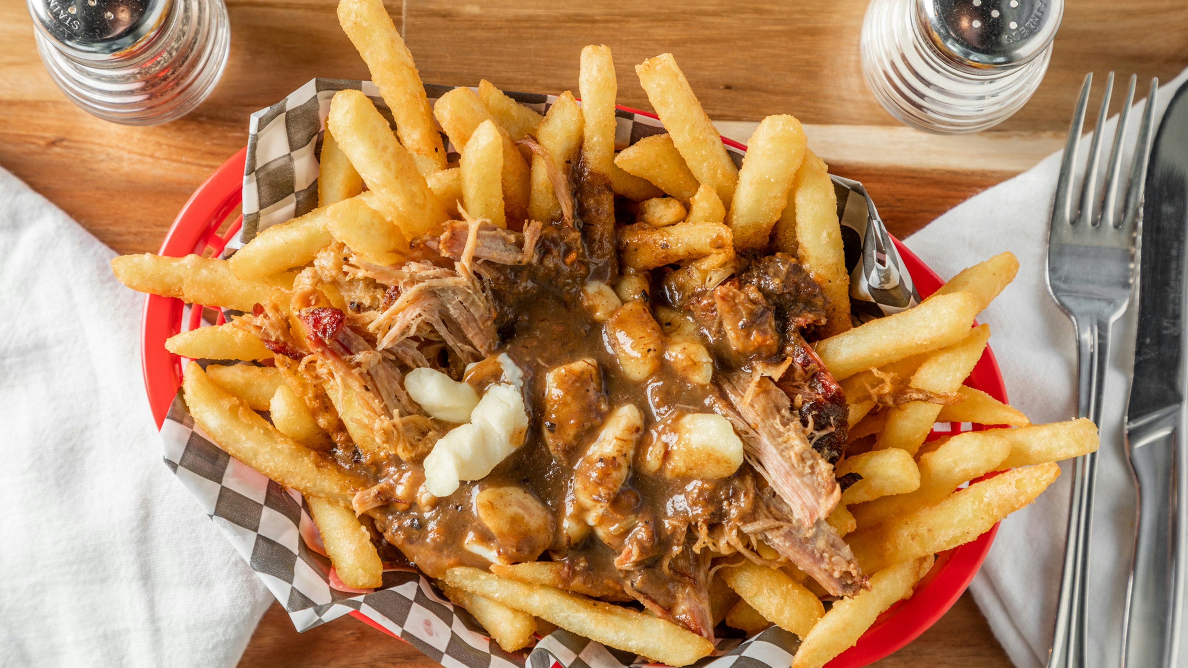 A shot of French fries and cheese curds topped with smoked brisket and sauce: a USA-style poutine.