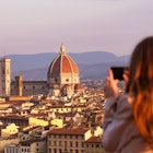 A woman taking a photo of the Florence skyline at sunset.