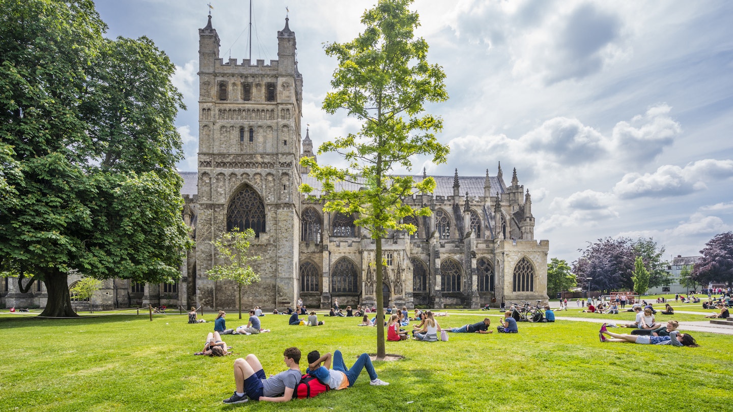 People relaxing on the green in front of Exeter Cathedral, Devon, England.