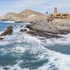 The Hacienda Cerritos Hotel sits on a rocky ocean-front outcropping as waves break on the rocks around it
1368299828