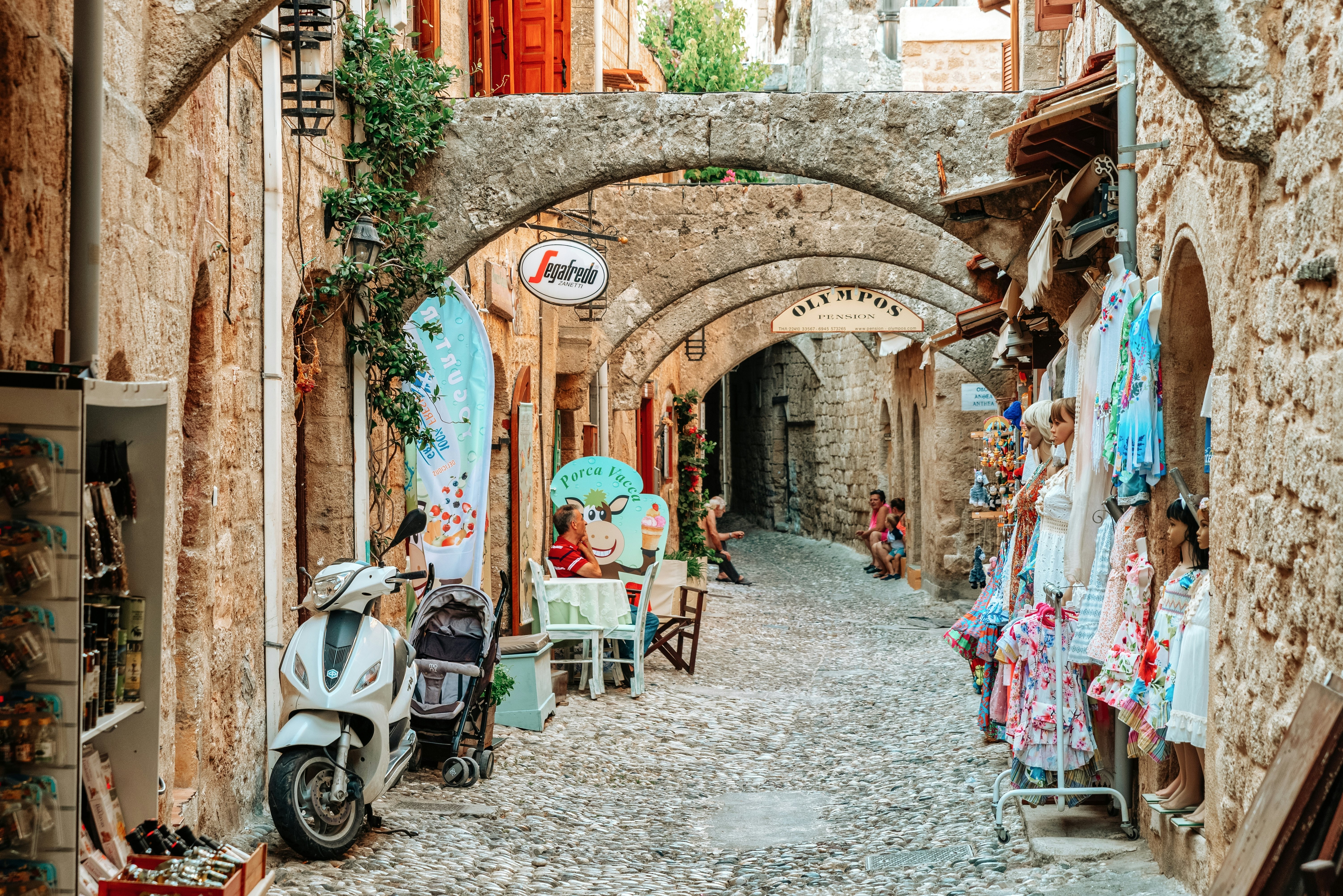 A narrow cobblestone street with shops and cafes housed in low stone buildings